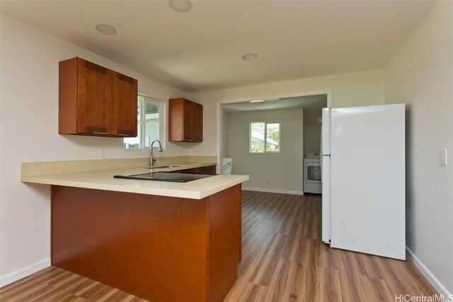 kitchen featuring light countertops, a sink, freestanding refrigerator, a peninsula, and wood finished floors