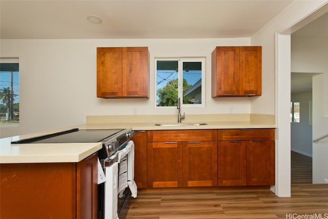 kitchen with stainless steel range with electric stovetop, light countertops, a sink, and brown cabinets