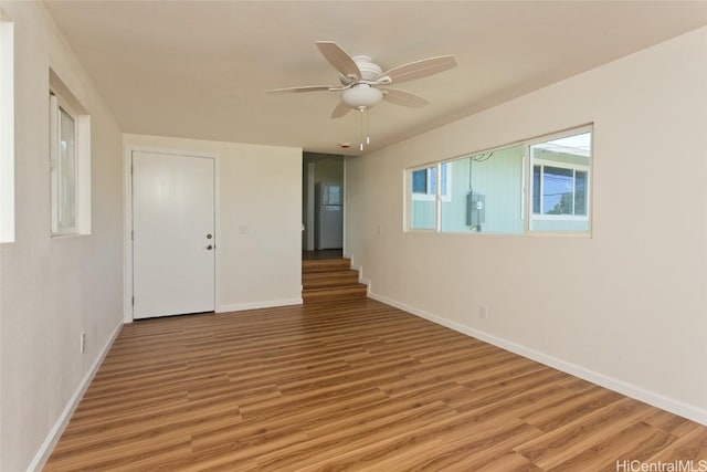 empty room featuring baseboards, light wood-type flooring, ceiling fan, and stairway
