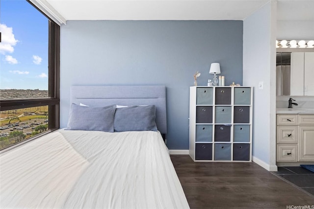 bedroom with ensuite bath, baseboards, a sink, and dark wood finished floors