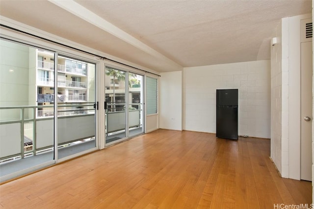 unfurnished room featuring a textured ceiling, concrete block wall, and wood finished floors