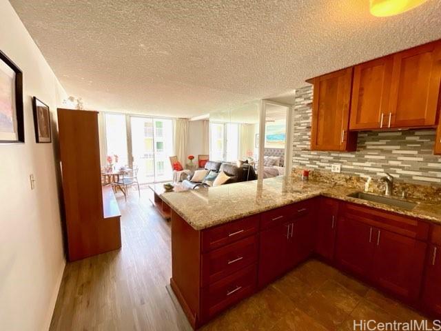 2452 Tusitala St Unit 703, Honolulu, HI 96815 - kitchen with a peninsula, backsplash, open floor plan, a textured ceiling, and light stone counters