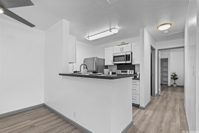 95-510 Wikao St Unit F206, Mililani, HI 96789 - kitchen with appliances with stainless steel finishes, white cabinetry, light wood-type flooring, dark countertops, and baseboards
