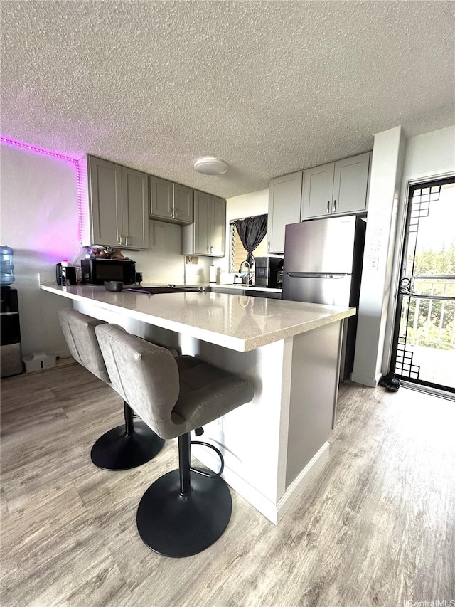 kitchen featuring light wood finished floors, appliances with stainless steel finishes, a kitchen breakfast bar, and a textured ceiling