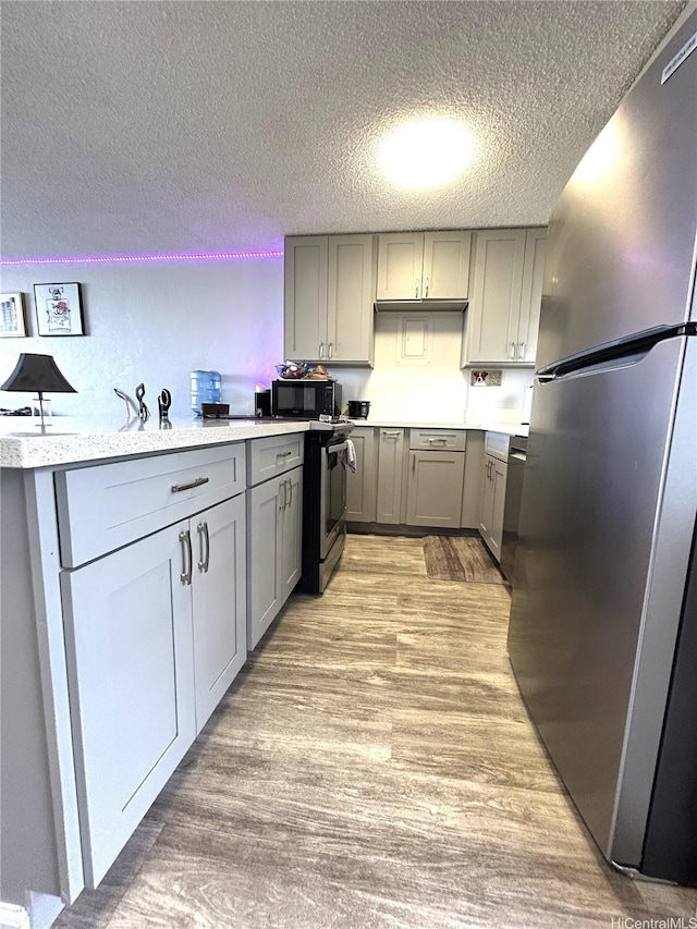 kitchen featuring light wood-type flooring, a textured ceiling, light countertops, gray cabinetry, and stainless steel appliances