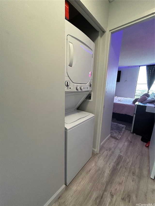 laundry area featuring stacked washing maching and dryer, laundry area, baseboards, and wood finished floors