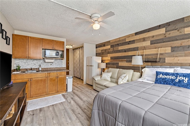 bedroom with wooden walls, freestanding refrigerator, light wood finished floors, and a textured ceiling