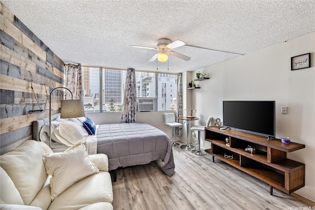 bedroom featuring a ceiling fan, a textured ceiling, wood finished floors, and cooling unit