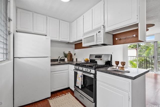 kitchen featuring white cabinets, dark countertops, a sink, and white appliances