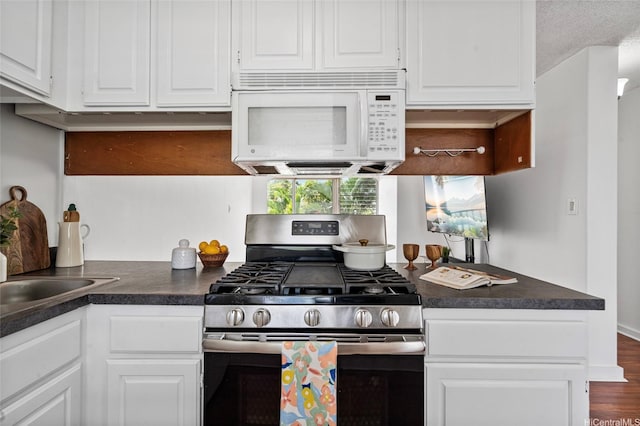 kitchen with white cabinets, dark countertops, gas range, and white microwave