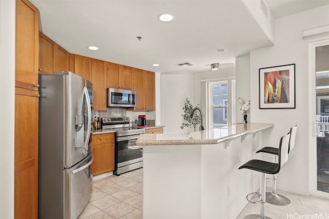kitchen featuring tasteful backsplash, a peninsula, visible vents, a breakfast bar area, and appliances with stainless steel finishes