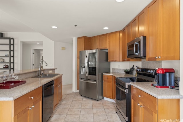 kitchen with light stone counters, recessed lighting, brown cabinetry, appliances with stainless steel finishes, and a sink
