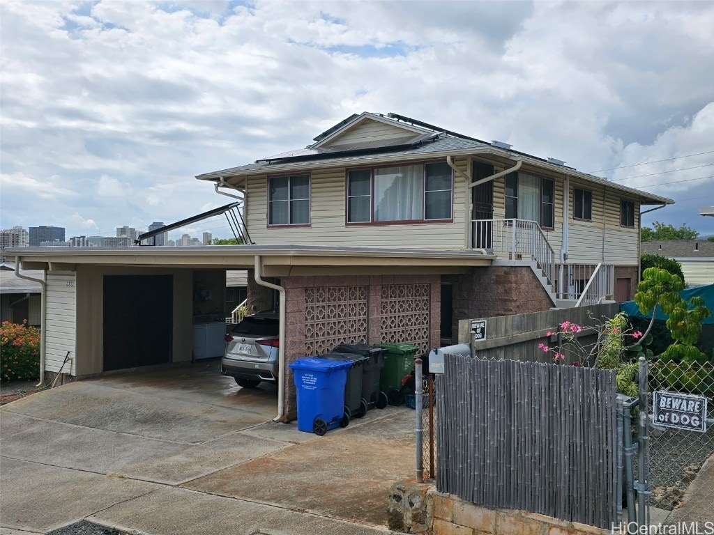 view of front of house featuring driveway, a gate, an attached carport, fence, and solar panels