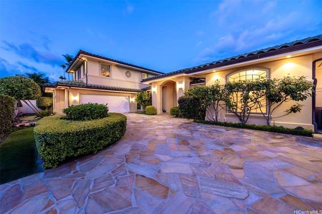 mediterranean / spanish-style house featuring a garage, driveway, stucco siding, and a tile roof