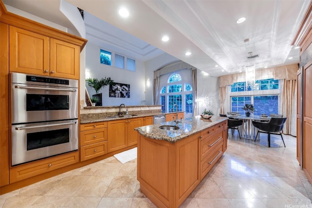 kitchen with stainless steel appliances, light stone countertops, a tray ceiling, and a sink