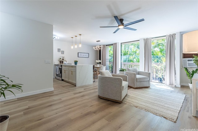living room with light wood-style floors, baseboards, ceiling fan with notable chandelier, and expansive windows