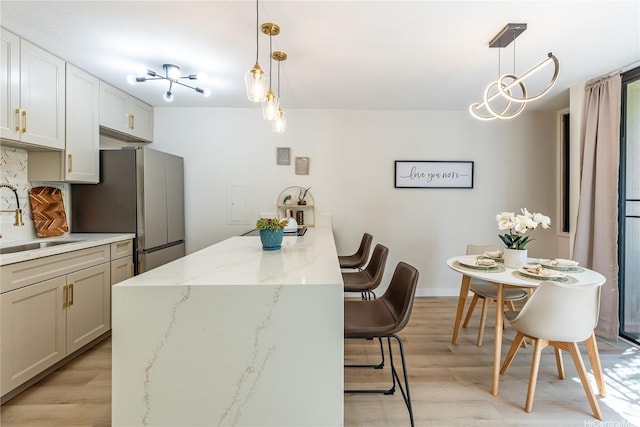kitchen with light wood-style floors, a sink, a breakfast bar area, and freestanding refrigerator