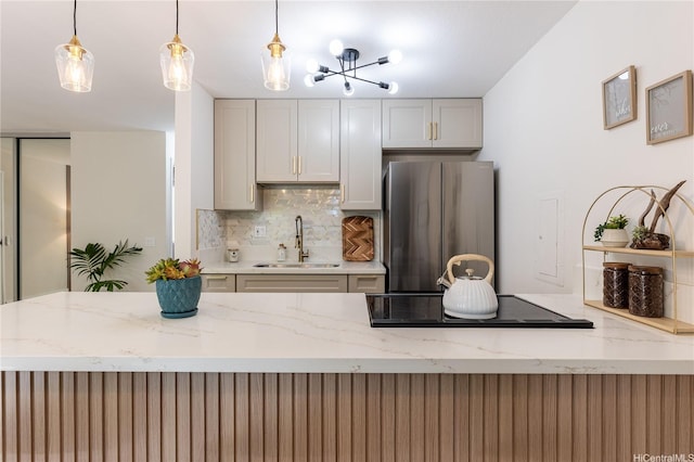 kitchen featuring black electric stovetop, a sink, freestanding refrigerator, decorative light fixtures, and decorative backsplash