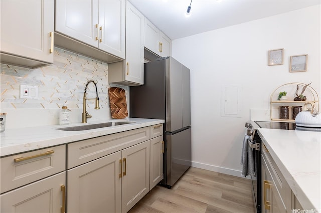 kitchen featuring baseboards, tasteful backsplash, a sink, light wood-style flooring, and appliances with stainless steel finishes