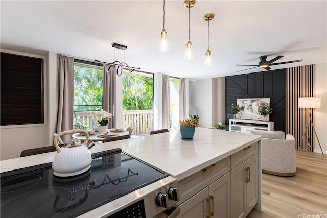 kitchen with light stone counters, light wood finished floors, a ceiling fan, pendant lighting, and range with electric stovetop