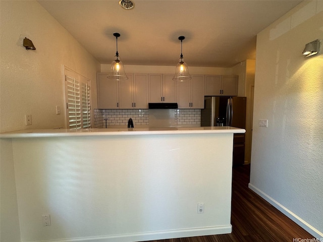 kitchen featuring decorative backsplash, light countertops, baseboards, under cabinet range hood, and dark wood-style floors