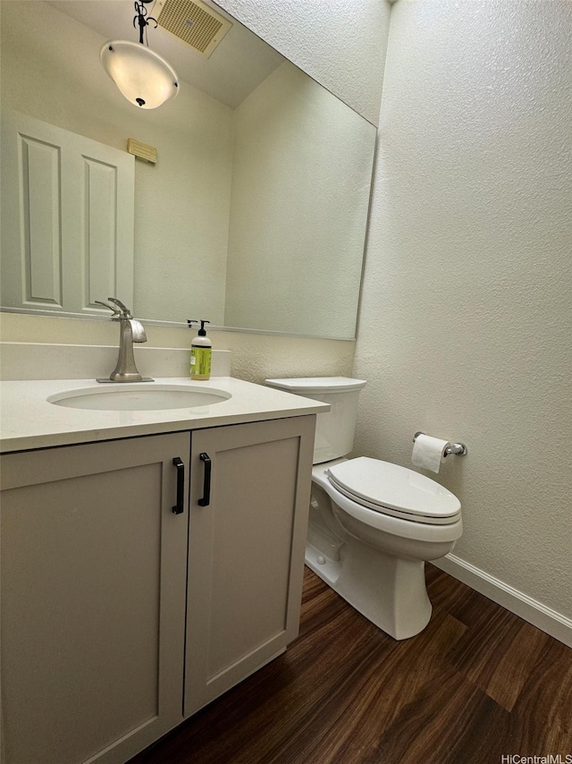 half bathroom featuring wood finished floors, vanity, baseboards, toilet, and visible vents