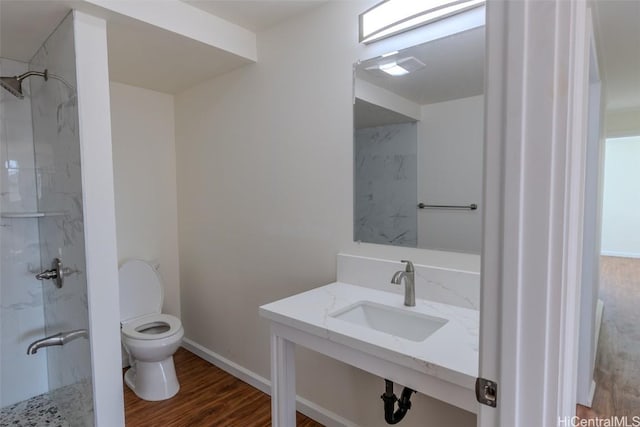 bathroom with a shower, baseboards, toilet, wood finished floors, and a sink