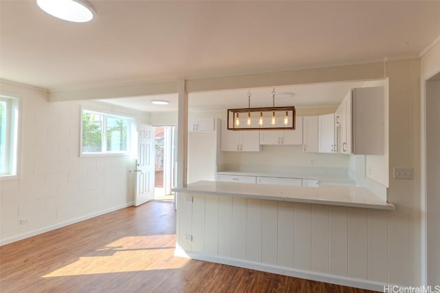 kitchen featuring light countertops, white cabinets, a peninsula, wood finished floors, and decorative light fixtures