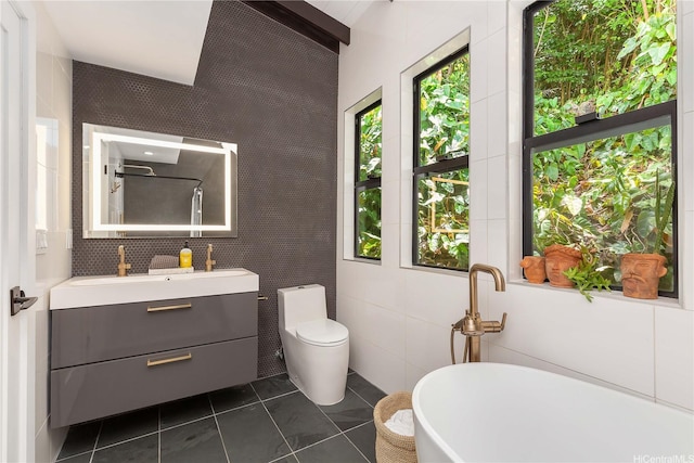 bathroom with tile patterned flooring, tile walls, toilet, vanity, and a soaking tub