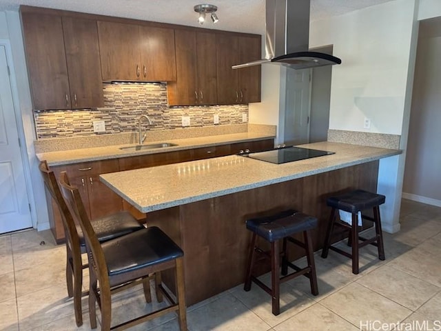 kitchen featuring tasteful backsplash, a sink, a breakfast bar area, black electric stovetop, and wall chimney exhaust hood