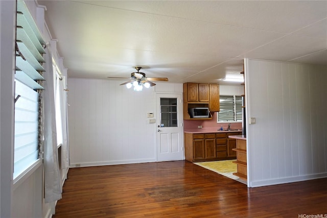 kitchen with dark wood-type flooring, brown cabinets, stainless steel microwave, and baseboards