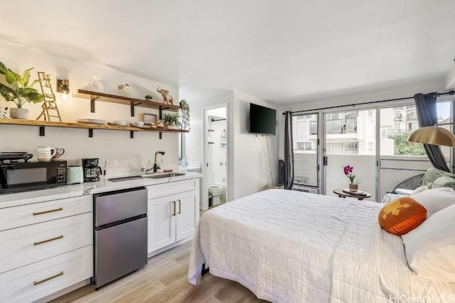 bedroom featuring light wood-style floors, freestanding refrigerator, a sink, and ensuite bath