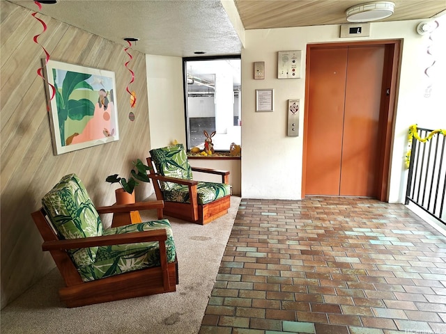 hallway with elevator, wood walls, brick patterned floors, and a textured ceiling