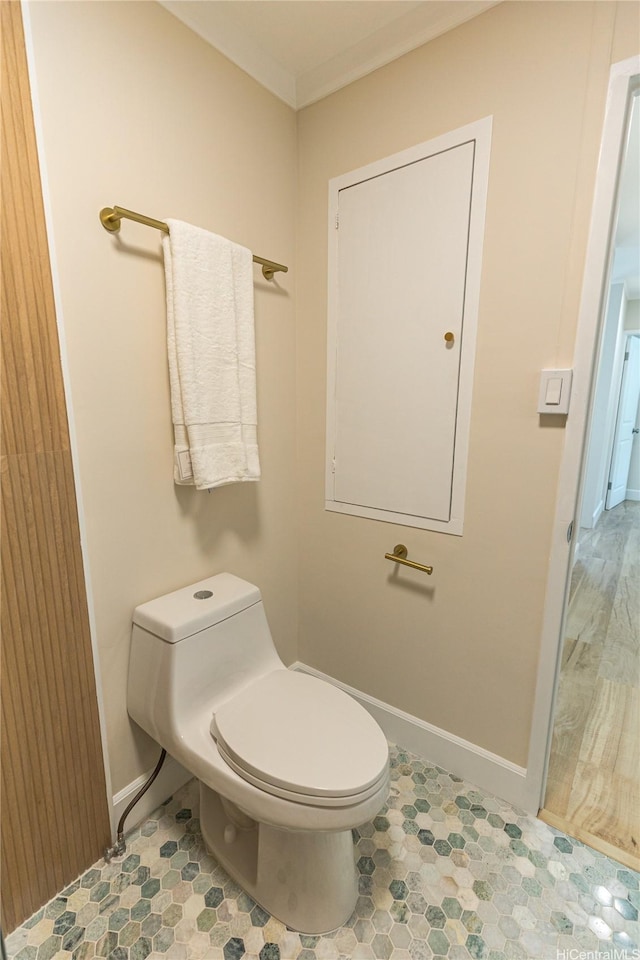 bathroom featuring baseboards, crown molding, and toilet
