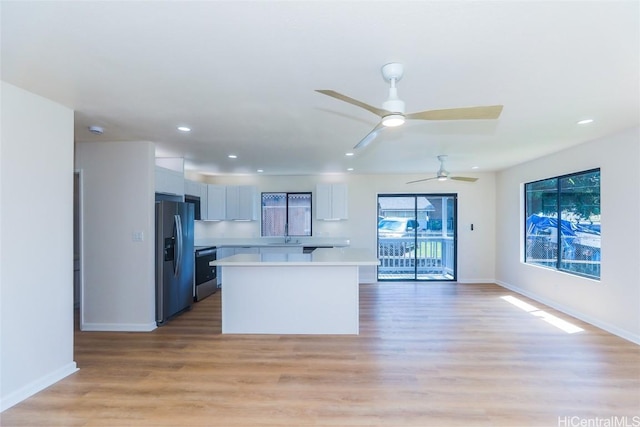 kitchen featuring light wood-style flooring, a center island, light countertops, stainless steel fridge, and baseboards