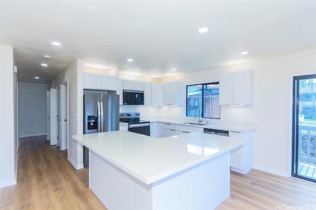 kitchen featuring a center island, light countertops, stainless steel appliances, light wood finished floors, and a sink