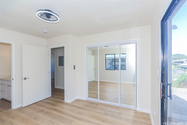 unfurnished bedroom with a closet, baseboards, light wood-type flooring, and electric panel