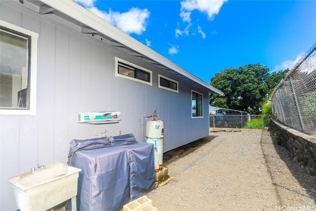 view of side of property featuring gas water heater, a sink, and fence