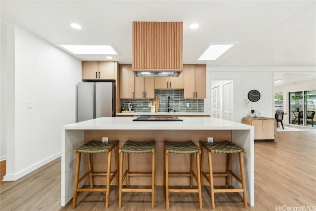 kitchen featuring freestanding refrigerator, tasteful backsplash, a skylight, light countertops, and light wood finished floors
