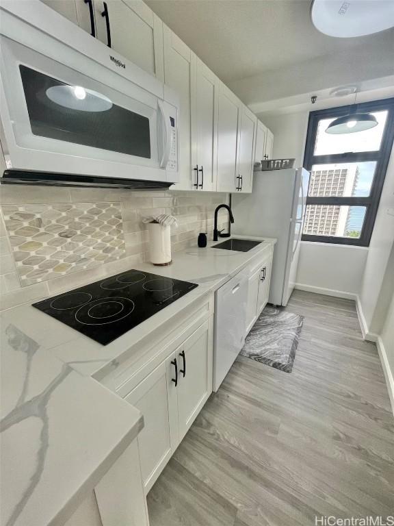kitchen featuring white appliances, white cabinetry, backsplash, light wood-style floors, and a sink