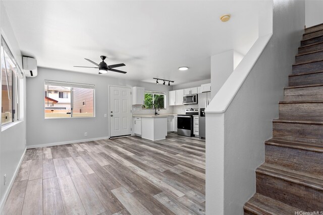 91-241 Makalauna Pl Unit 15, Ewa Beach, HI 96706 - unfurnished living room with a wall mounted air conditioner, stairway, light wood finished floors, and ceiling fan