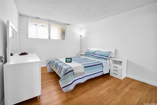 2211 Ala Wai Blvd Unit 1106, Honolulu, HI 96815 - bedroom featuring light wood-style flooring, a textured ceiling, concrete block wall, and baseboards