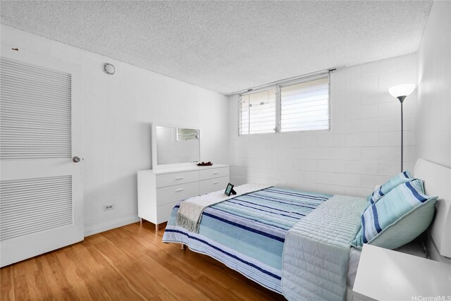 2211 Ala Wai Blvd Unit 1106, Honolulu, HI 96815 - bedroom featuring wood finished floors, a textured ceiling, concrete block wall, and baseboards