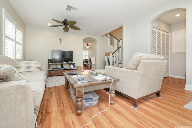 living room featuring arched walkways, ceiling fan, wood finished floors, stairs, and baseboards