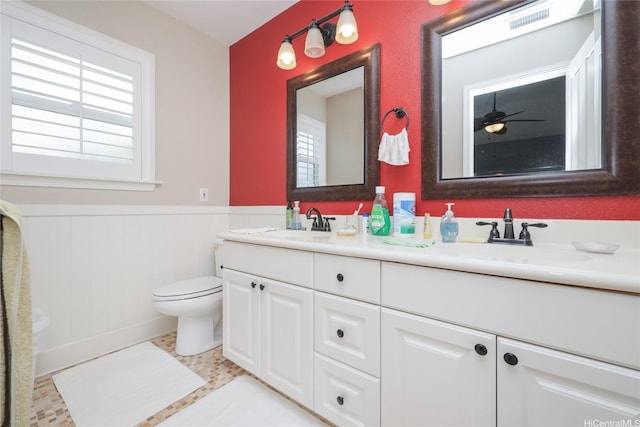 bathroom featuring a wainscoted wall, toilet, plenty of natural light, and double vanity