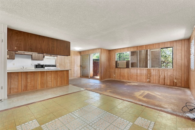 kitchen with tile patterned floors, wooden walls, extractor fan, a sink, and stainless steel microwave