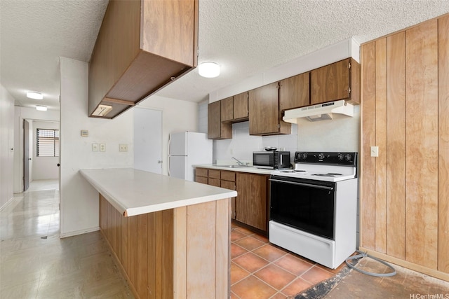 kitchen featuring black microwave, range with electric stovetop, a peninsula, under cabinet range hood, and freestanding refrigerator