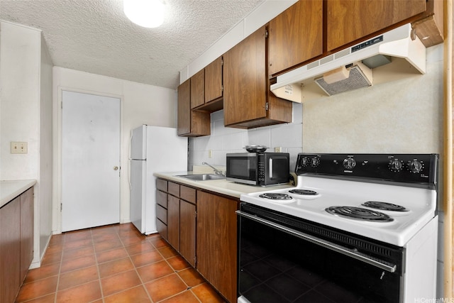 kitchen featuring range with electric stovetop, under cabinet range hood, light countertops, a sink, and freestanding refrigerator