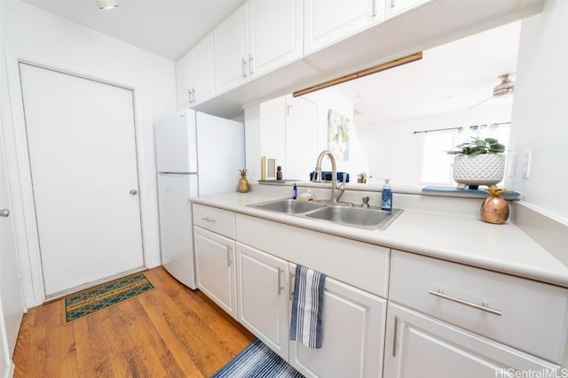 kitchen featuring a sink, light wood-type flooring, white cabinets, and freestanding refrigerator
