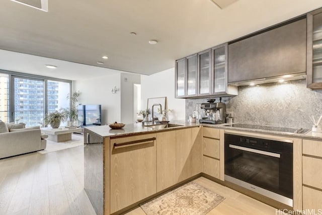 kitchen with black electric stovetop, oven, light brown cabinetry, and a sink